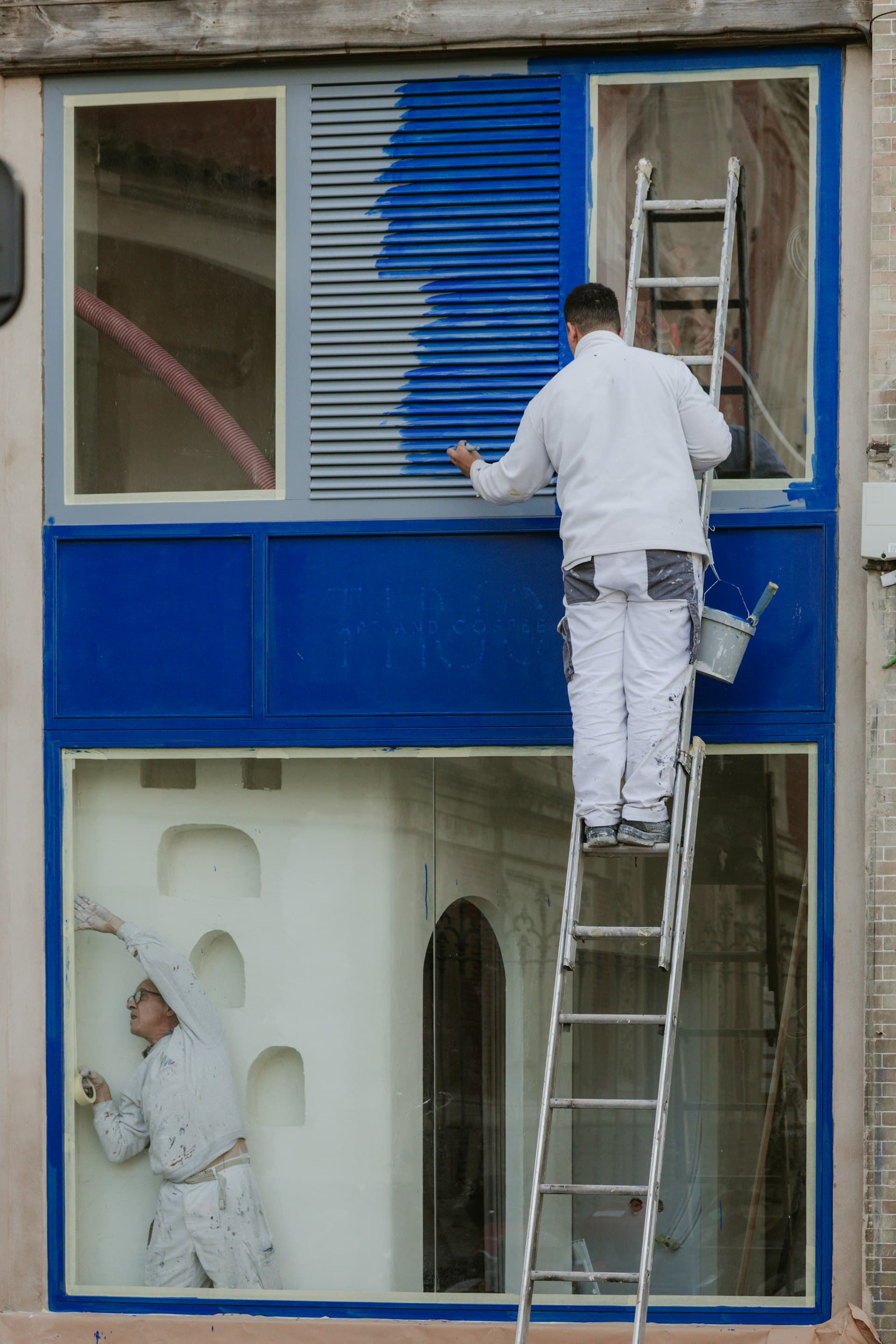 Peintre en bâtiment sur échelle peignant une fenêtre